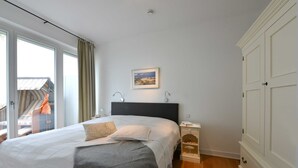 A bedroom with a large bed, a nightstand, a wardrobe, and a window with curtains. - Herring Gull, Germany (Sassnitz)