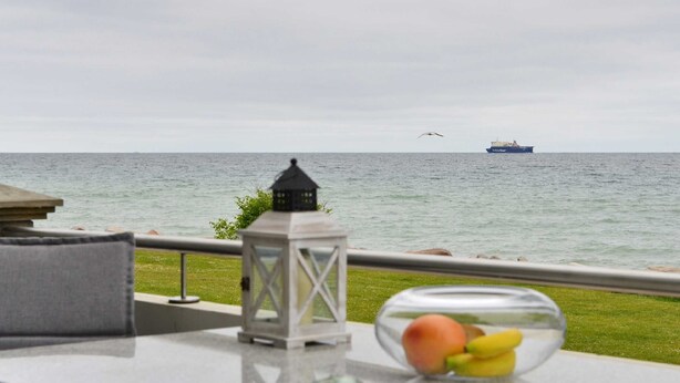 A balcony with a view of the sea, a ship in the distance, and a glass table with fruit and a bottle. - Herring Gull, Germany (Sassnitz)