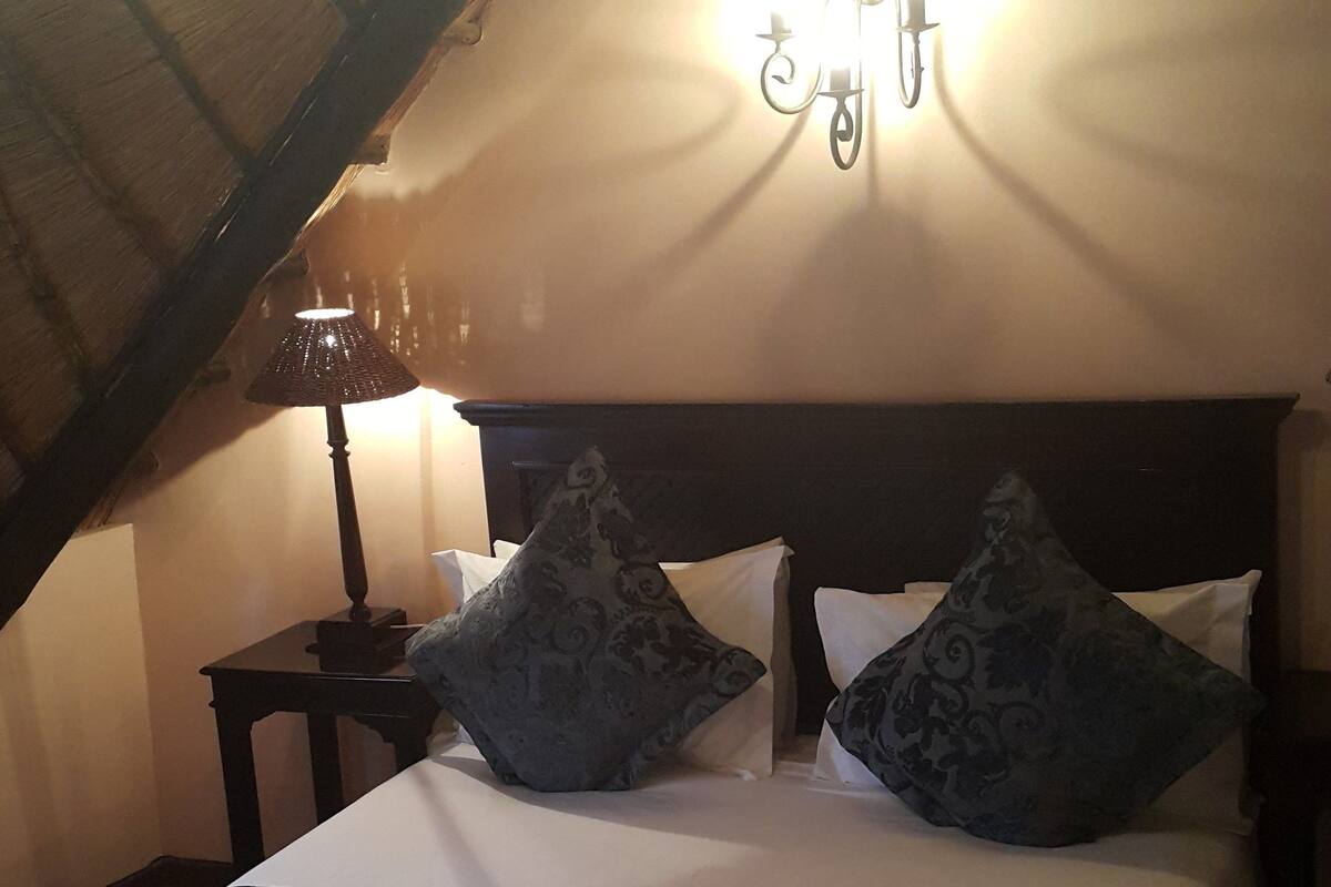 A bedroom with a bed, two pillows, a nightstand, a lamp, and a wall-mounted light fixture.