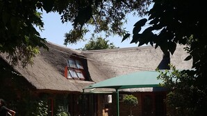 Un bâtiment traditionnel à toit de chaume, doté d’un patio couvert et entouré de verdure.