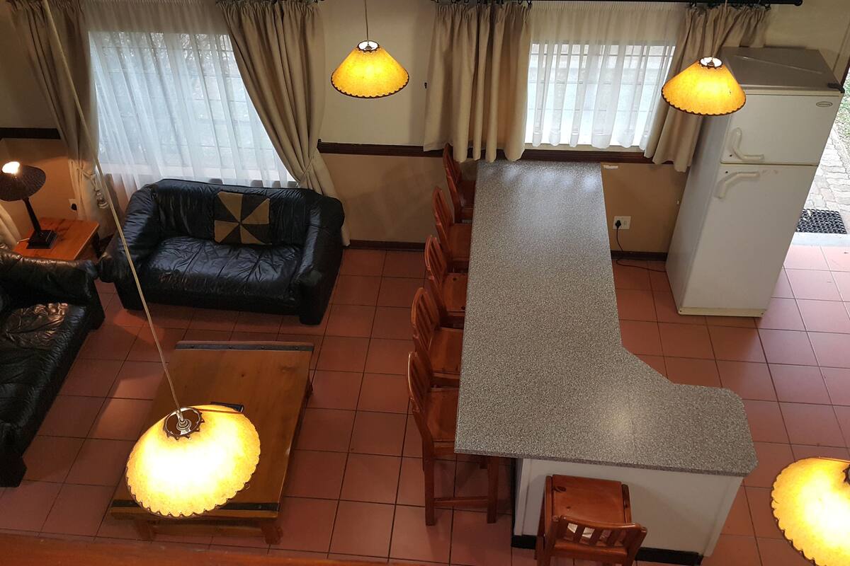 A living room with a black leather sofa, a wooden coffee table, and a kitchen area with a granite countertop and wooden chairs.