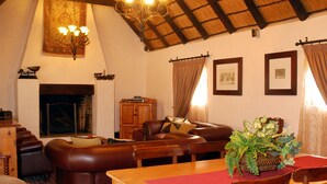 Un salon chaleureux avec une cheminée, des meubles en cuir et un coin repas agrémenté d’une nappe rouge.