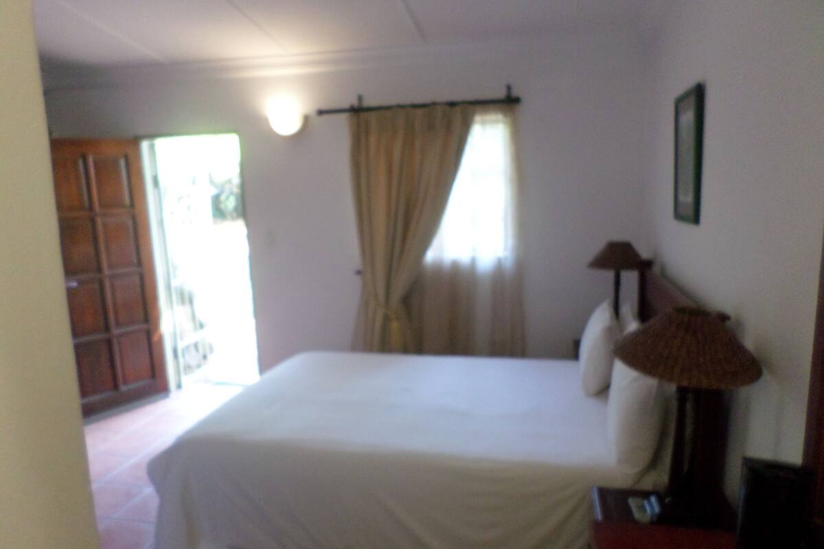 A bedroom with a bed, a nightstand, a lamp, and a window with curtains.