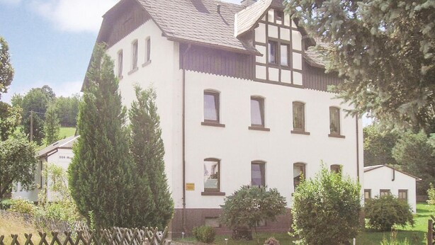 Un bâtiment à deux étages, doté d’une façade blanche et de bordures sombres. Il présente de nombreuses fenêtres et un toit en pente.
