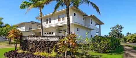 A two-story house with a stone wall in front, surrounded by well-maintained grass and tropical plants.