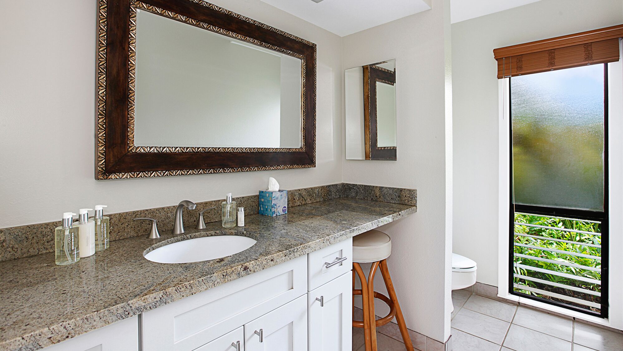 A bathroom with a granite countertop, a white sink, a large mirror, and a toilet.