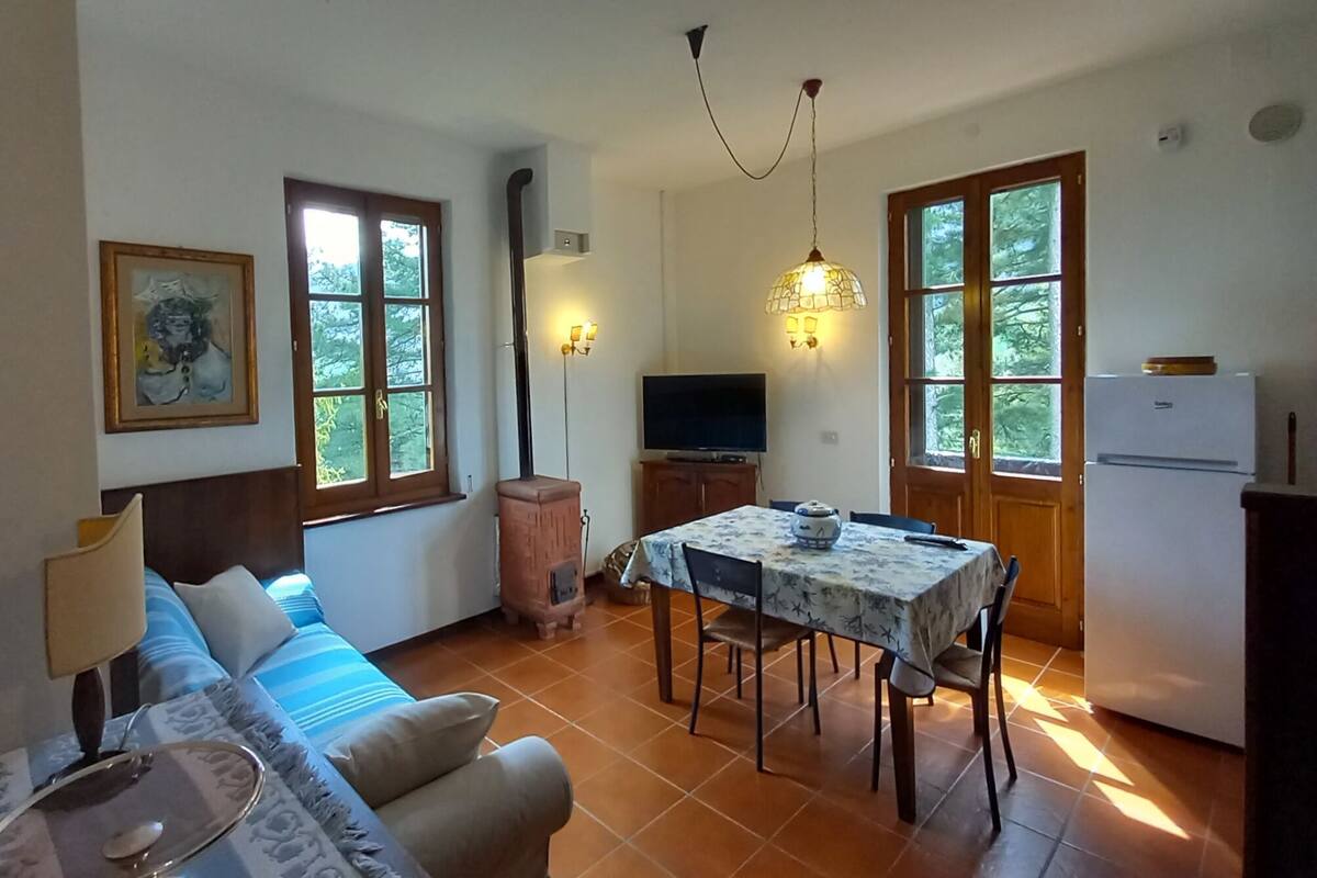 A living room with a sofa, a dining table with chairs, a television, and a kitchen area with a refrigerator.
