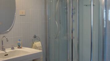 Une salle de bain avec une douche à parois de verre, un lavabo avec un miroir et des articles de toilette posés sur le comptoir.