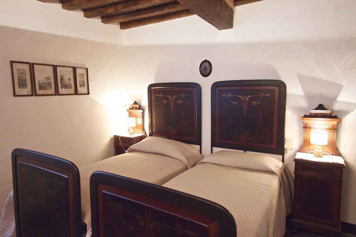 A double bed with wooden headboards, a bedside table with a lamp, and framed pictures on the wall.