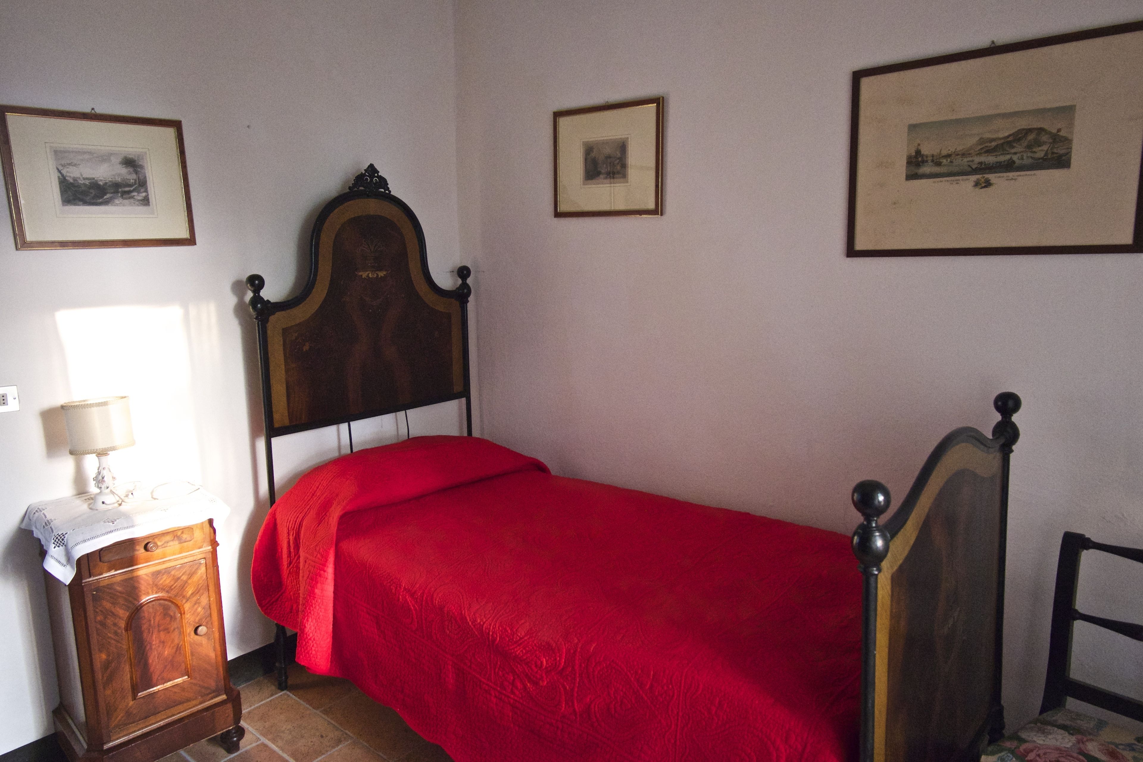 Un dormitorio con una cama de madera, una mesita de noche con una lámpara y tres cuadros enmarcados en la pared.