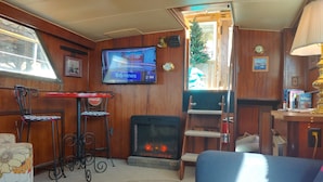 A cozy living room with a television, a fireplace, a Coca-Cola branded stool, and a patterned rug.