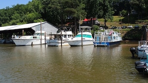A marina with several boats docked, a covered area, and a building with a red roof in the background.