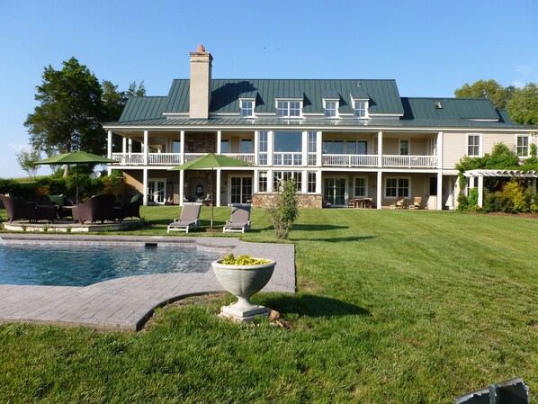 A large two-story house with a swimming pool, outdoor seating, and a well-maintained lawn.