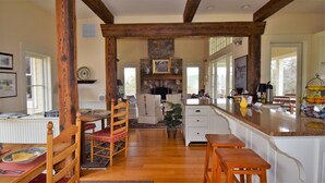 Una cocina amplia con vigas de madera, chimenea de piedra y comedor con sillas y mesa.