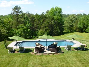 A swimming pool with lounge chairs and umbrellas, surrounded by a grassy lawn and trees.