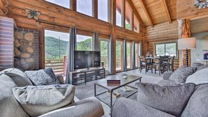 A spacious living room with a fireplace, large windows, and a television. - Spacious Hilltop Cabin w/ Deck & Scenic Views! (Eden)