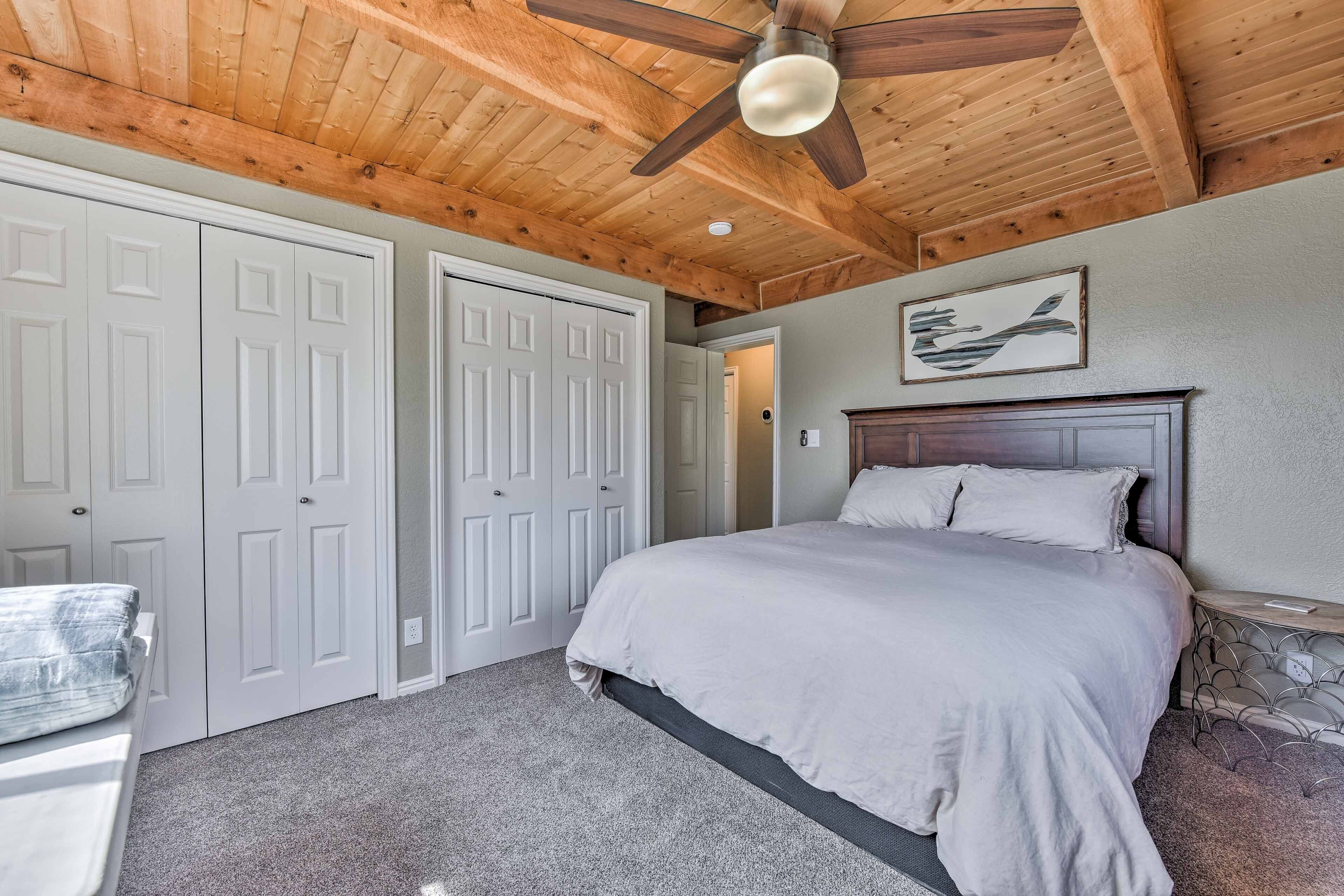 A bedroom with a bed, white closets, a ceiling fan, and a framed picture on the wall.