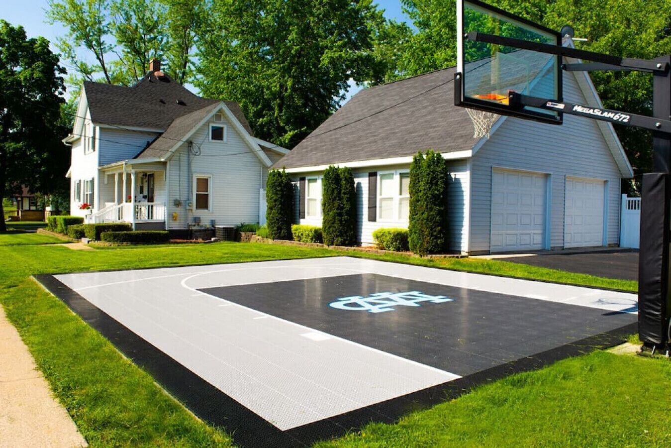 Une propriété résidentielle comprenant un terrain de basketball, un garage et une maison dotée d’un porche.