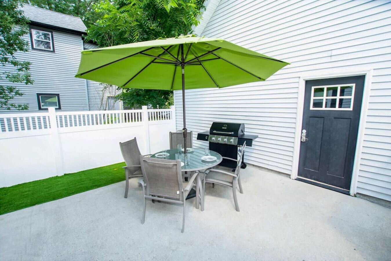 Une terrasse avec une table et des chaises en verre, un parasol vert et un barbecue.