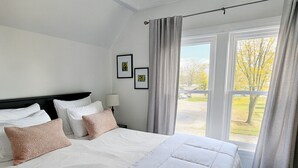 A hotel room with a large bed, a nightstand, a lamp, and a window with curtains. - Field House | Game Room | DOWNTOWN Dells | Basketball Court| Arcade (Wisconsin Dells)