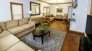 A living room with a beige sofa, a coffee table, a patterned rug, a television, and a bookshelf with decorative items. - Field House | Game Room | DOWNTOWN Dells | Basketball Court| Arcade (Wisconsin Dells)