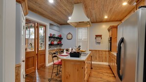A kitchen with wooden flooring, a central island, wooden cabinets, a refrigerator, and a window with blinds. - Historic Hot Springs Home < 1 Mi to Oaklawn! (Hot Springs)