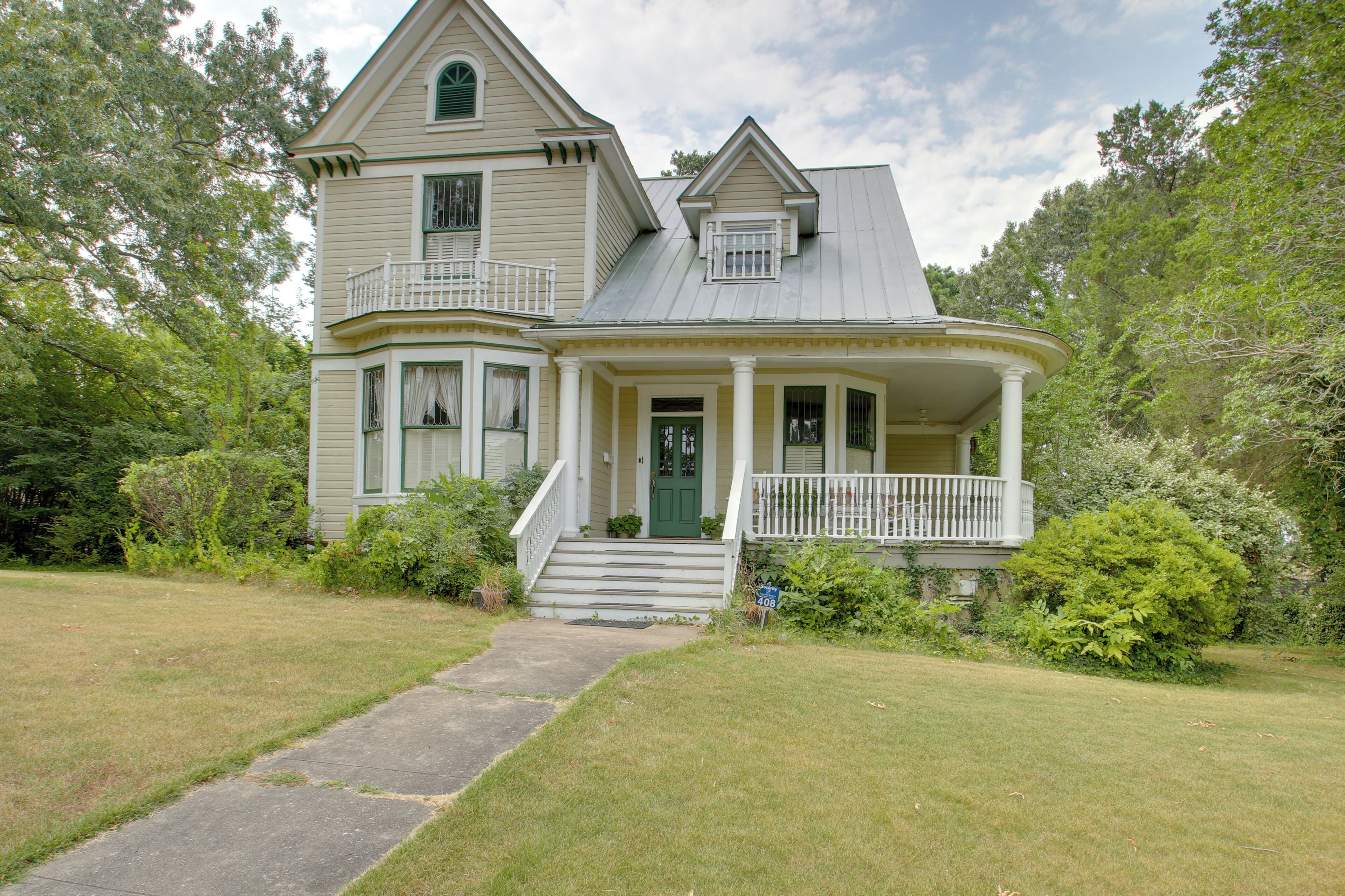 Une maison à deux étages avec une véranda qui fait le tour de la maison, une entrée avec une porte verte et un petit balcon au deuxième étage.