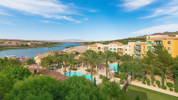 A resort with a pool area, palm trees, and a view of a lake and mountains.
