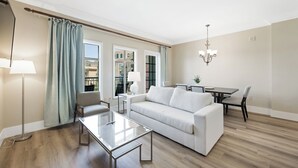 A modern living room with a white sofa, glass coffee table, and a dining area with a table and chairs.