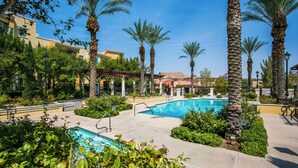A pool area with palm trees, a clear blue sky, and a building with a tiled roof in the background.