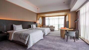 A hotel room with two beds, a desk, a chair, a large window, and a view of the city.