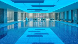 Una piscina interior moderna con paredes de vidrio transparente, suelo de baldosas y iluminación azul.