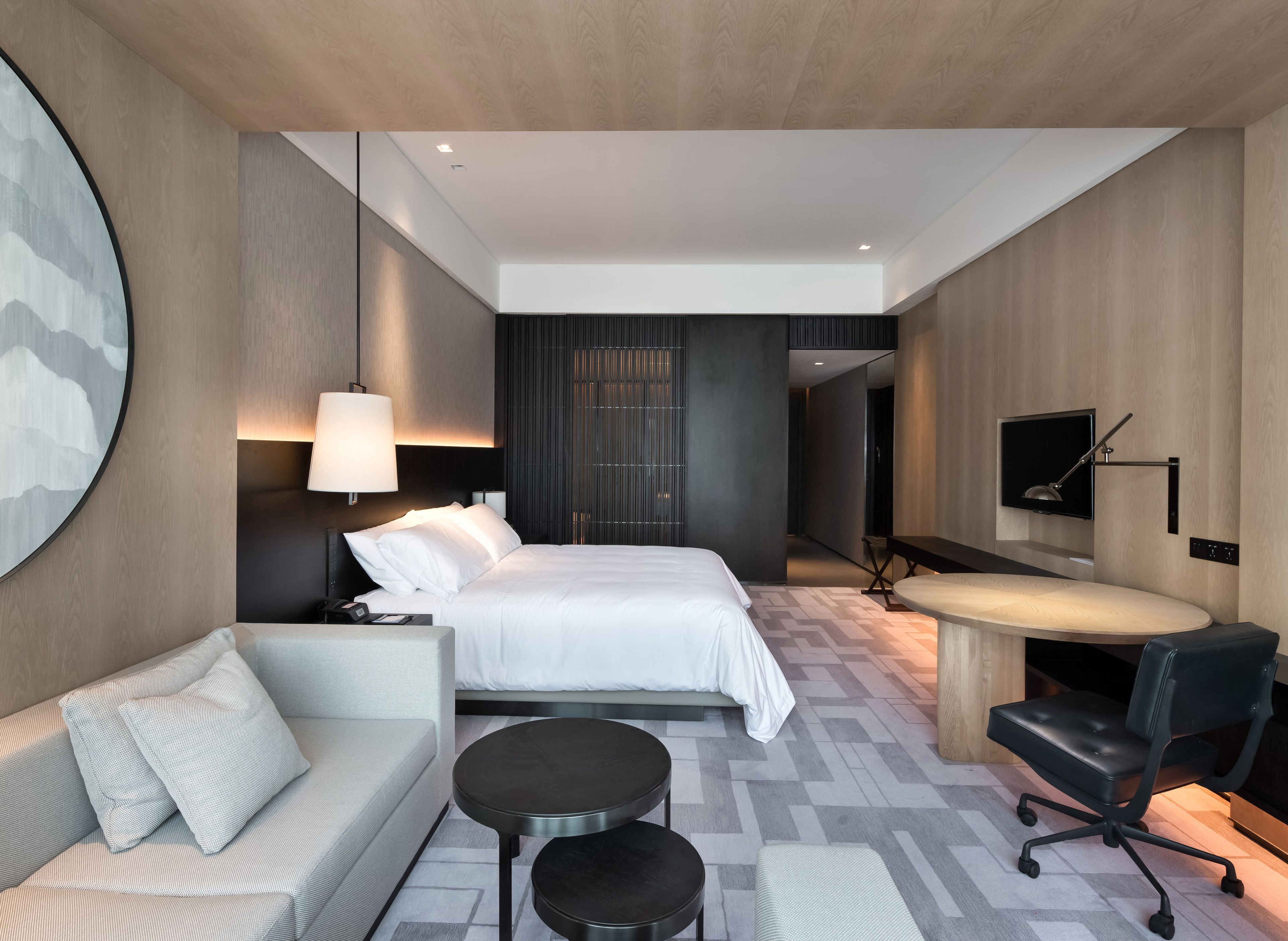 A modern hotel room with a bed, a desk, a chair, a sofa, and a TV.