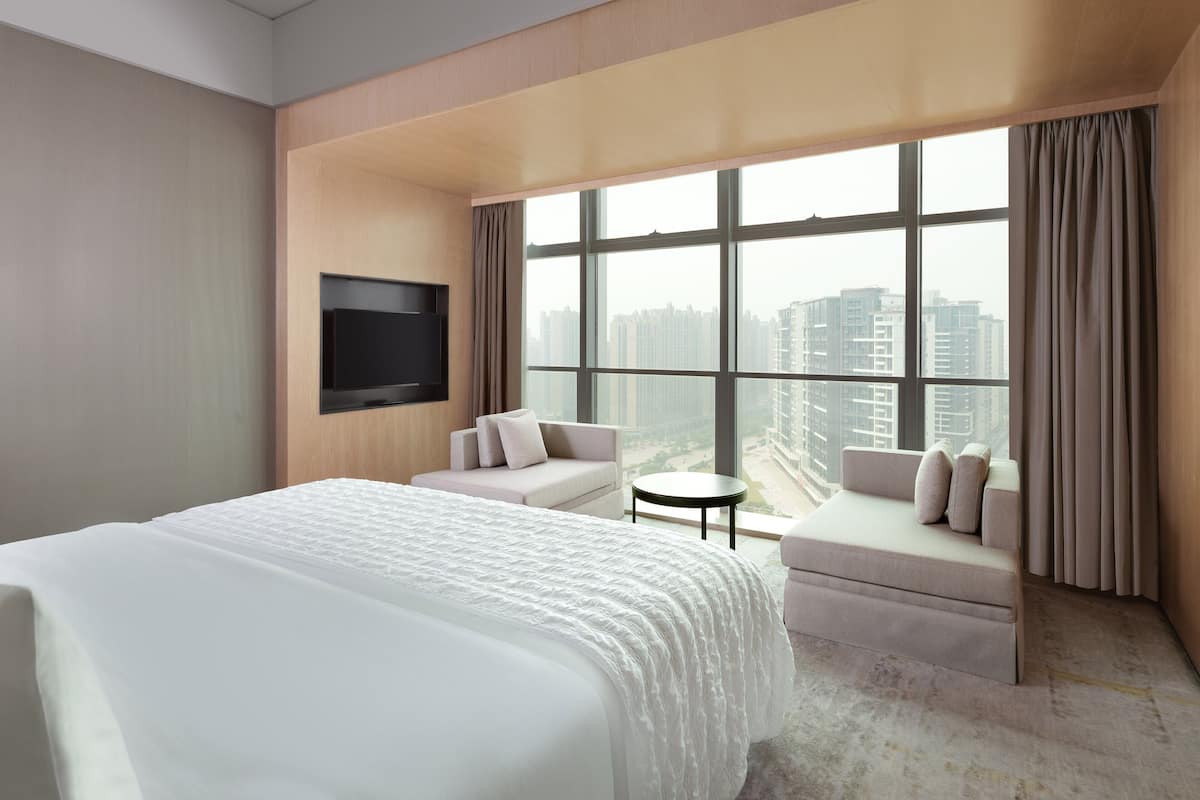 Una habitación de hotel moderna con una cama grande, un sofá, una pequeña mesa redonda y un televisor fijado a la pared.