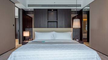 A modern hotel room with a large bed, a bedside table with a lamp, and a large mirror.