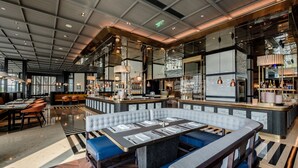 Un restaurante moderno con zona de bar, techos altos y una variedad de opciones de asientos, incluyendo cabinas y mesas.