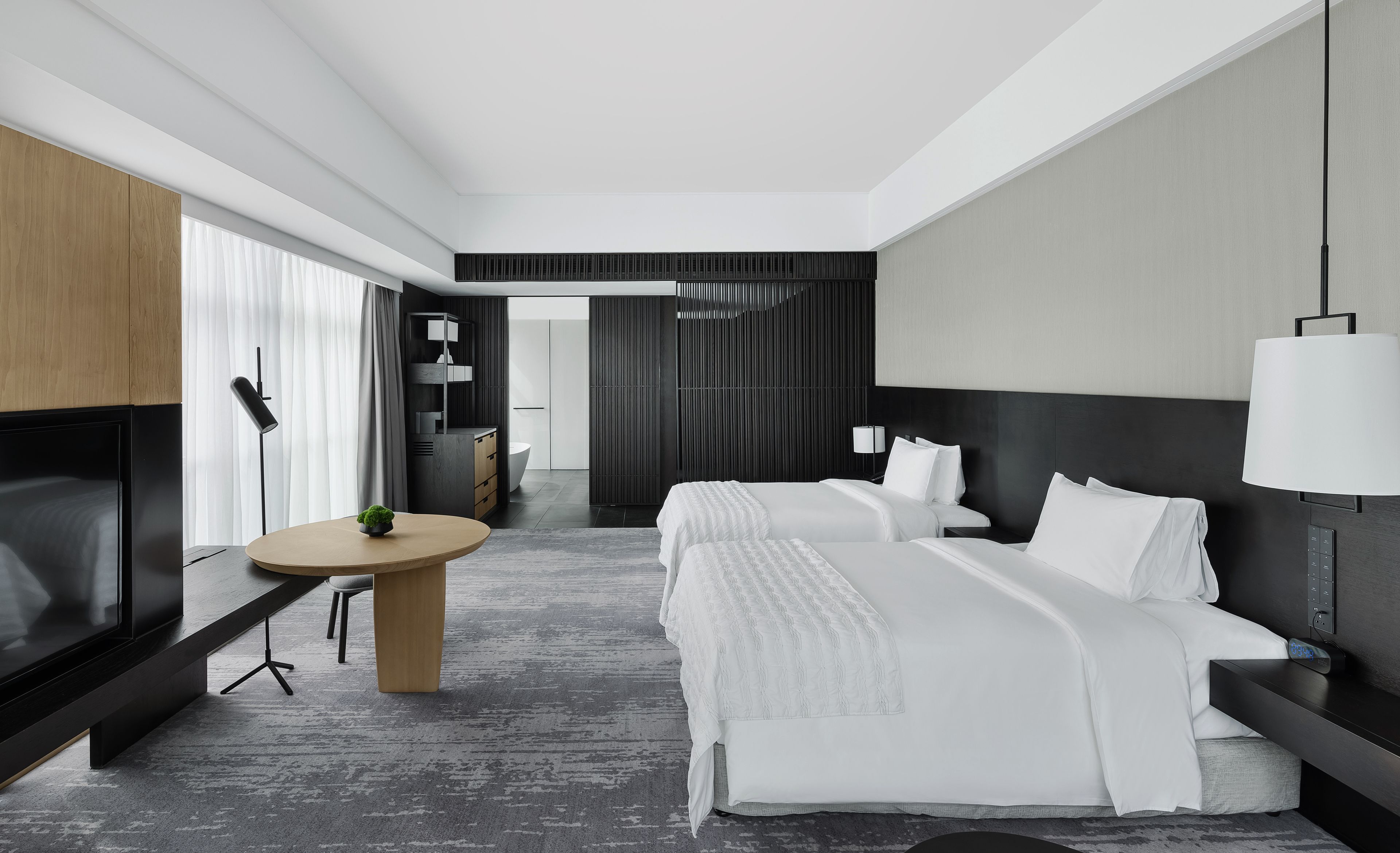 A modern hotel room with a large bed, bedside tables, a TV, and a desk with a chair.