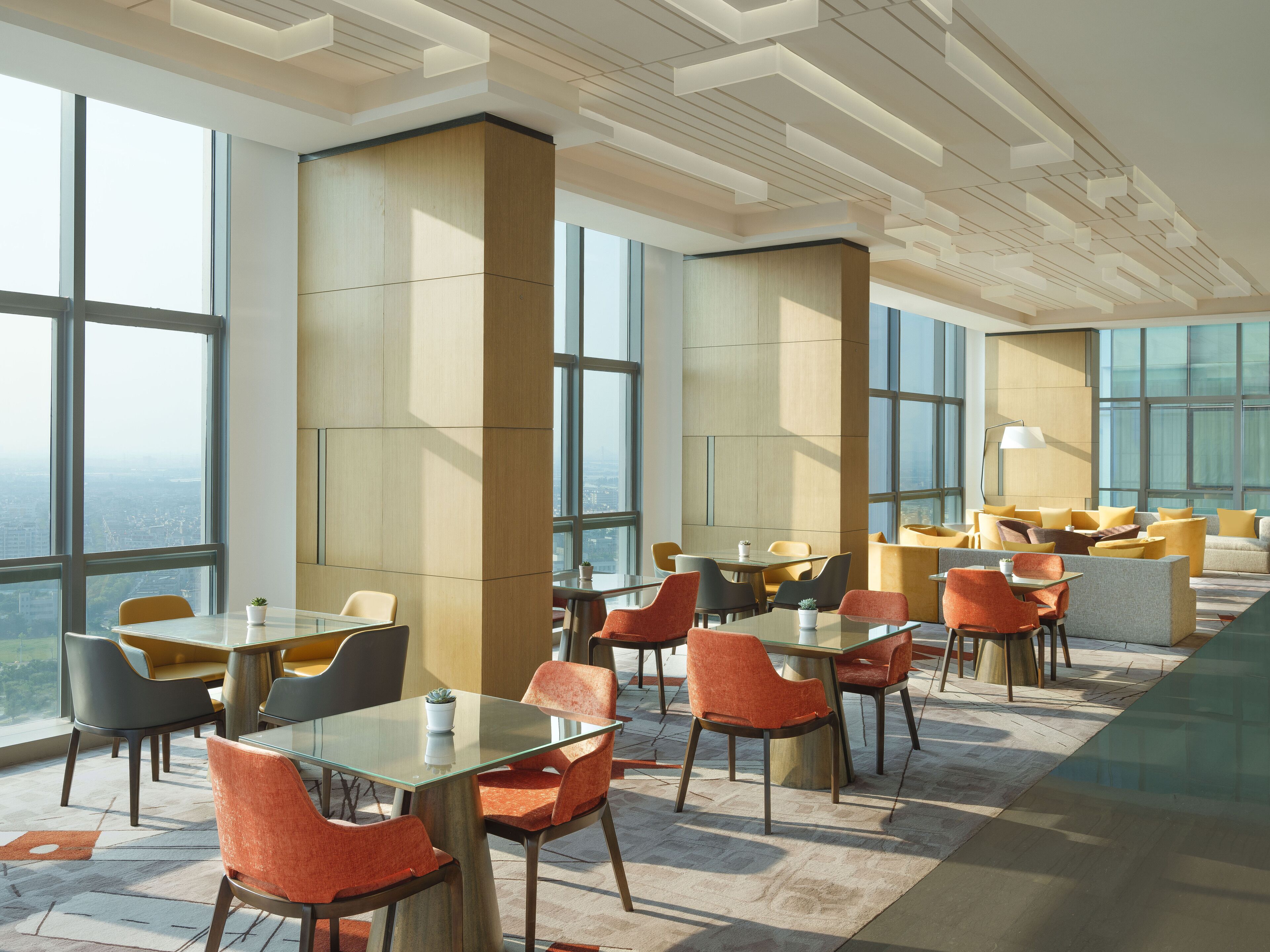 A modern hotel lobby with large windows, high ceilings, and a mix of seating arrangements including tables and chairs.