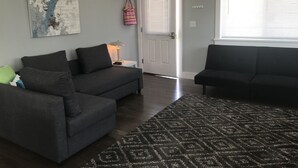 Ein Wohnzimmer mit zwei grauen Sofas, einem gemusterten Teppich und einer Tür zu einem weiteren Raum.