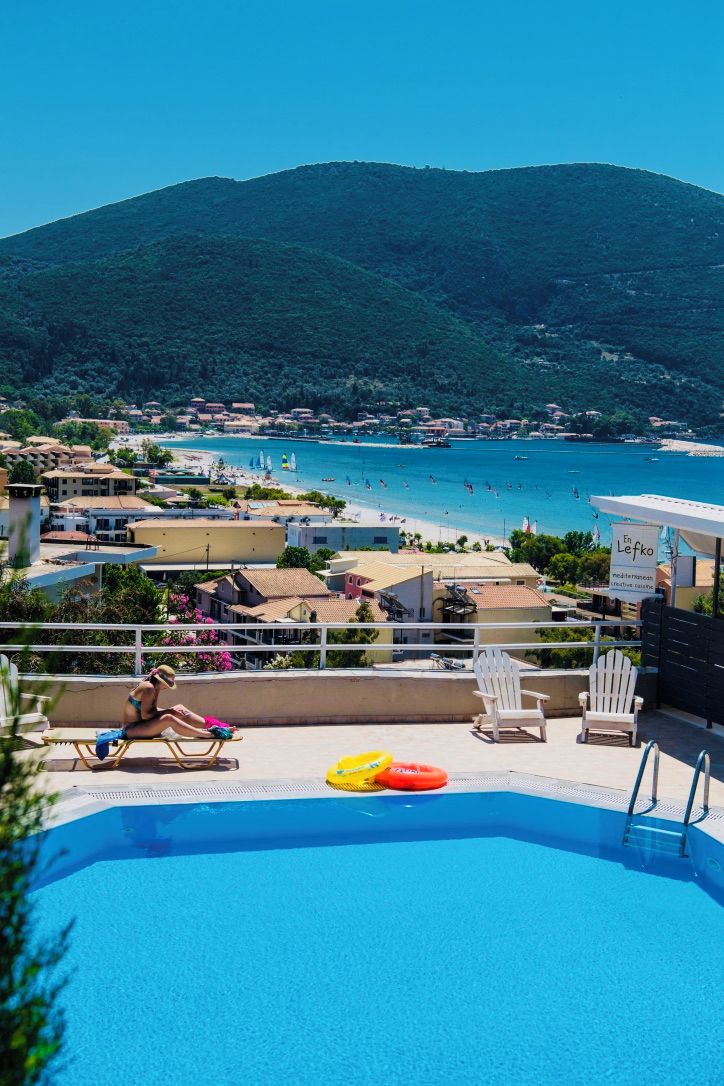 A swimming pool with lounge chairs, a view of a beach, and a mountain in the background.