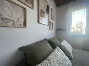 A room with a bed, a window with blinds, and framed artwork on the wall.