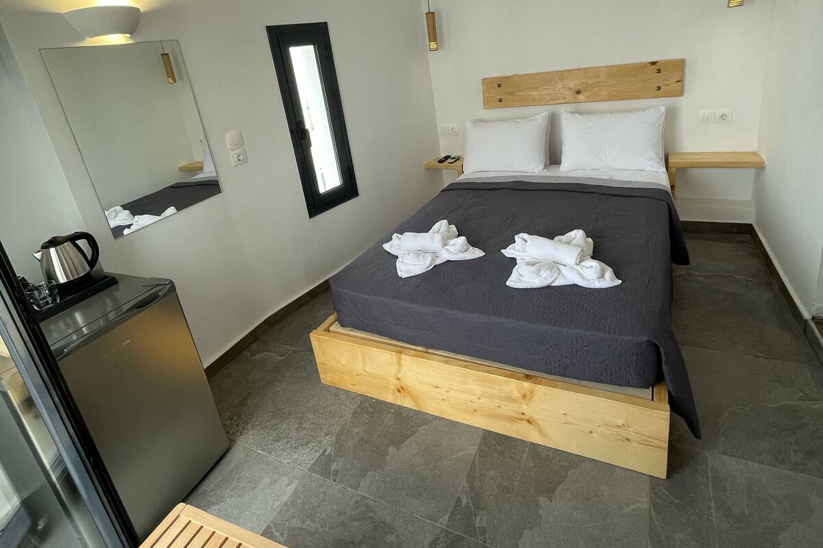 Un dormitorio con cama, mesita de noche y un escritorio pequeño con hervidor.