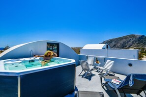 A rooftop terrace with a hot tub, lounge chairs, and a view of the mountains. - Sun Springs (Santorini)