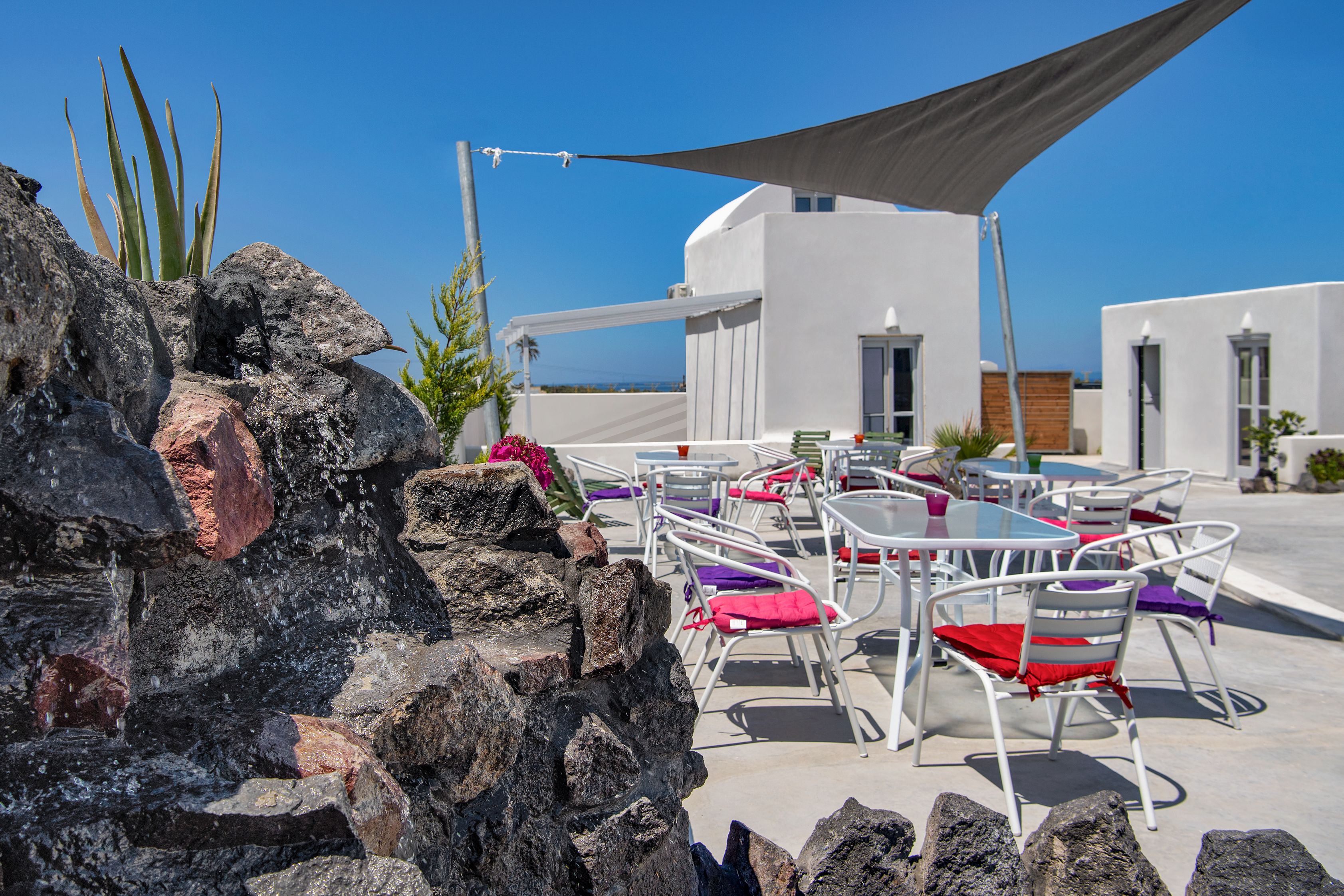 Una terraza con mesas al aire libre, un edificio blanco y un cielo azul despejado.
