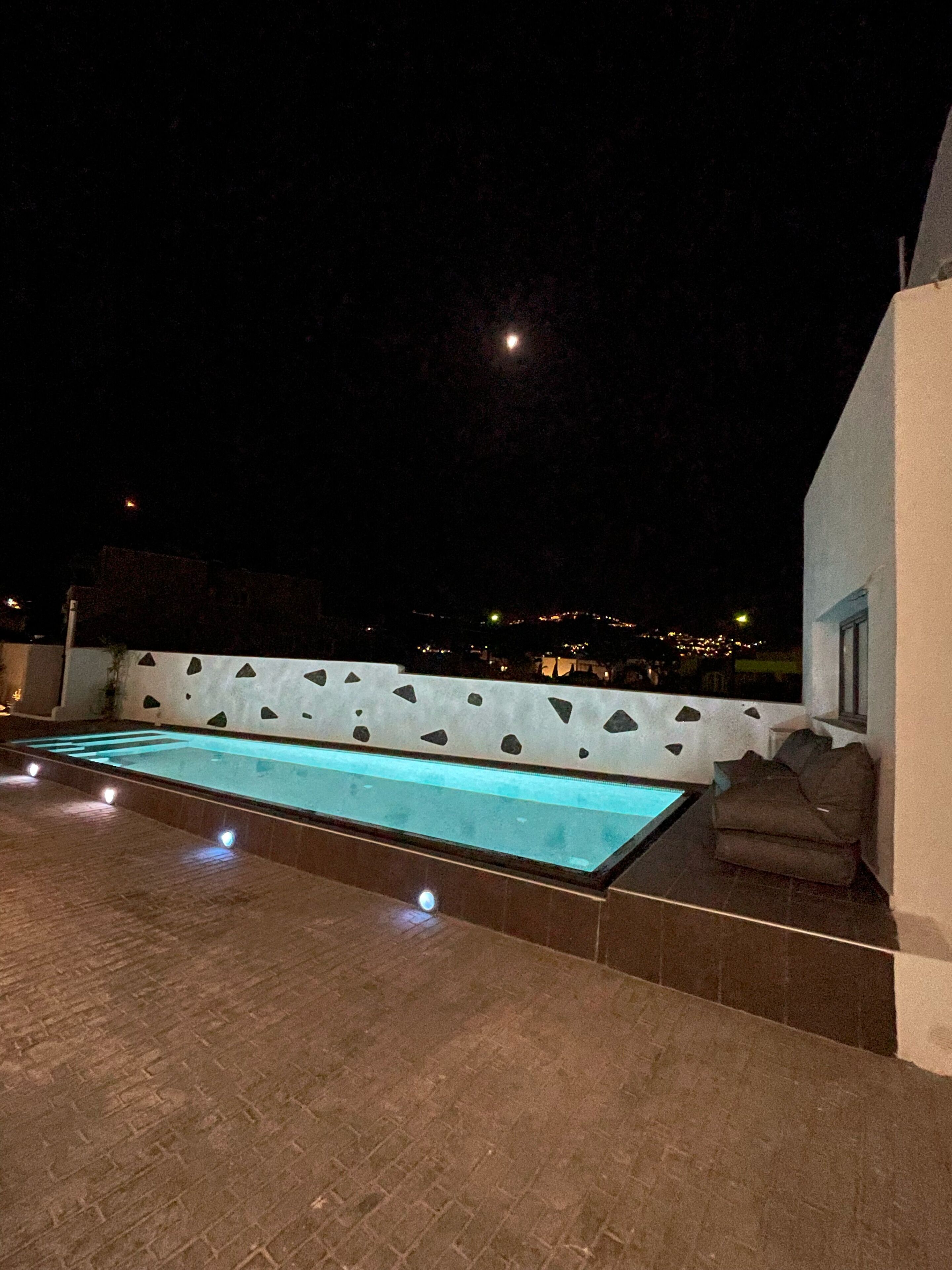 A rooftop pool area with a clear view of the night sky and city lights in the distance.