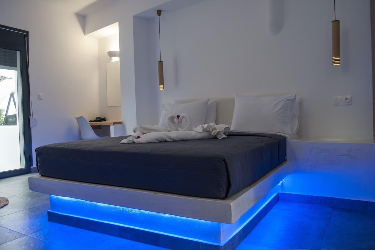 Un dormitorio moderno con una cama, mesitas de noche e iluminación azul en una plataforma.