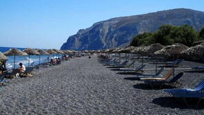 Una playa con filas de tumbonas y sombrillas, terreno rocoso y un acantilado grande al fondo.