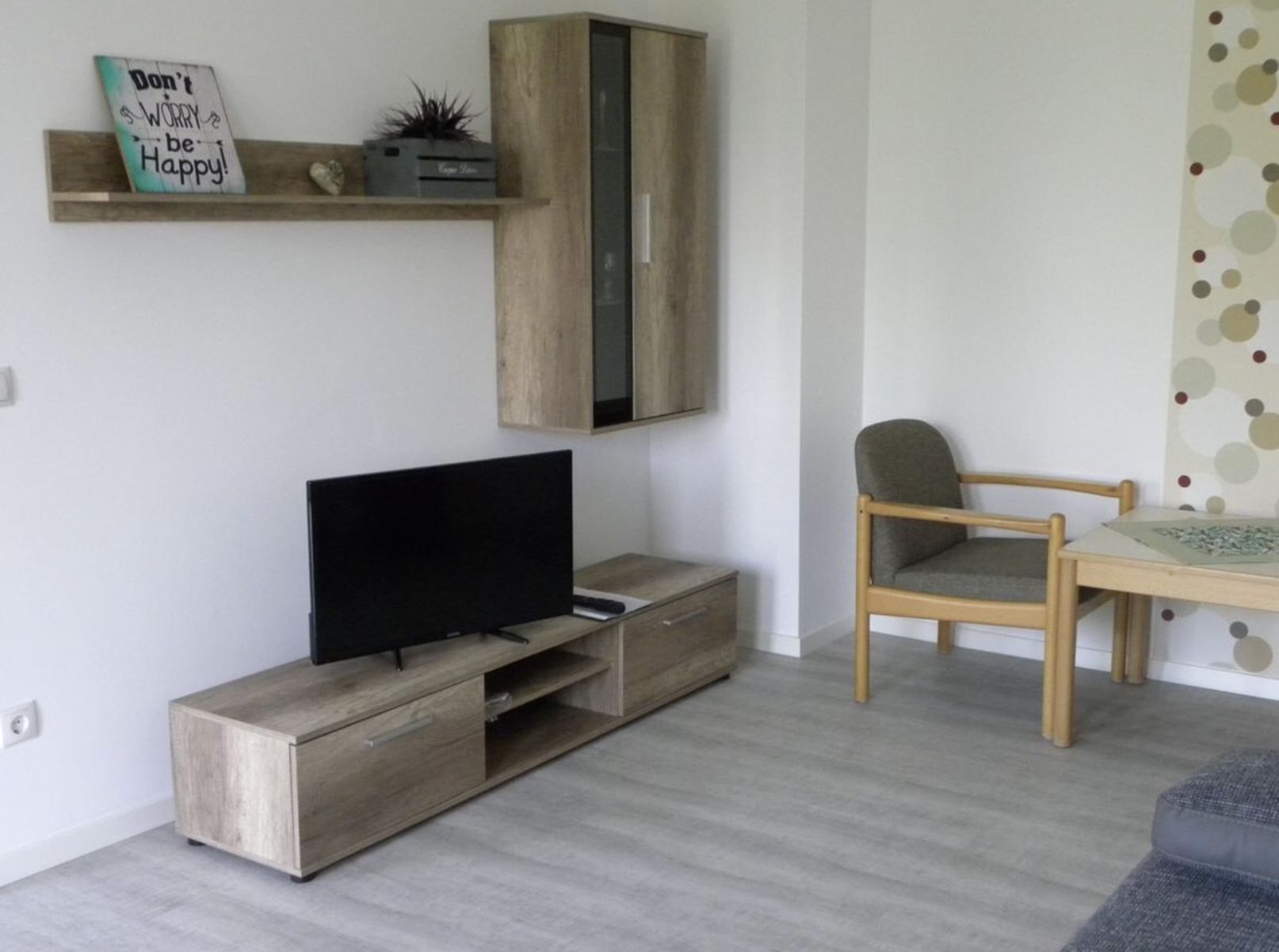 Una sala de estar moderna con un mueble de madera, un televisor de pantalla plana, un sofá gris y una silla de madera.