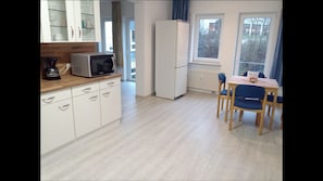 A modern kitchen with white cabinets, a microwave, and a refrigerator. There is a dining area with a table and chairs. - Appartemens Haus Maria Anna (Bad Ems)