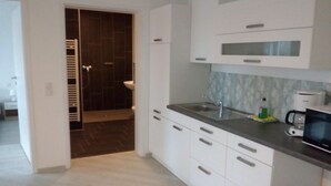 A modern kitchen with white cabinets, a stainless steel sink, and a microwave. - Appartemens Haus Maria Anna (Bad Ems)